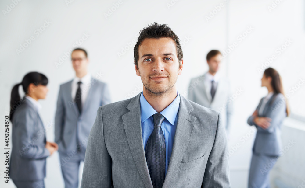 Hes part of a dynamic business team. Portrait of a handsome young businessman with his colleagues standing in the background. Hes part of a dynamic business team. Portrait of a handsome young businessman with his colleagues standing in the background.