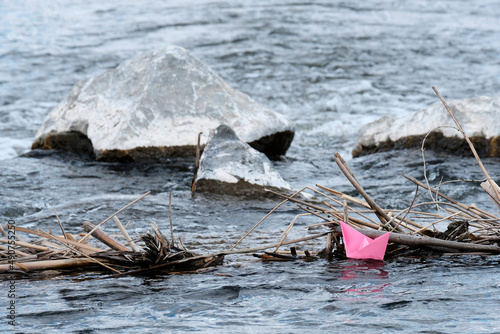 A paper boat, handmade, pink, red, floats in a spring puddle, water. The concept of the change of seasons.