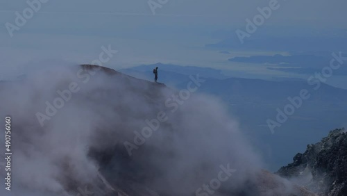Silhouette of man hiking at coldera of Avachinsky stratovolcano, also known as Avacha Volcano. Backpacker tourist moves upon rocks behind steam from hot geysers. Kamchatka Peninsula, Russia.