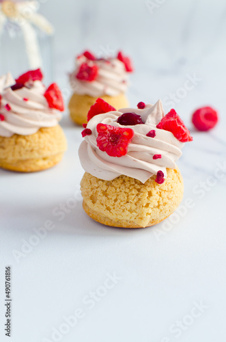 mini eclairs with cream and fresh raspberries on a light background