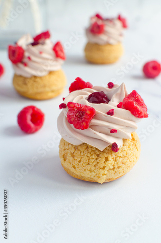 mini eclairs with cream and fresh raspberries on a light background