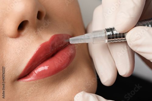 Young woman undergoing procedure of permanent lip makeup in salon, closeup