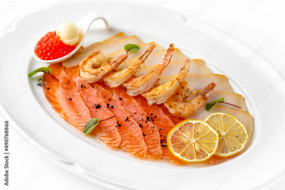 Plate with appetizer of fish and seafood. Sliced salted fish fillet. Smoked salmon, perch, prawn. Banquet festive dishes. Gourmet restaurant menu. White background. Plate with appetizer of fish and seafood. Sliced salted fish fillet. Smoked salmon, perch, prawn. Banquet festive dishes. Gourmet restaurant menu. White background.