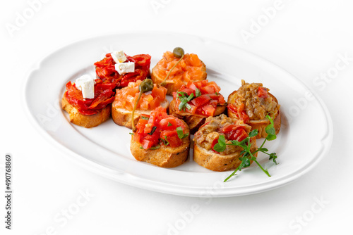 Mini bruschetta with salmon and capers, eggplant caviar, tomatoes and roasted peppers on a white plate