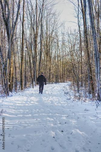 A man walking on a snowy trail, after the first snow, in a wooded area