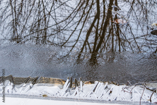 A relaxing scene of the river bank starting to freeze and reflecting the winter trees