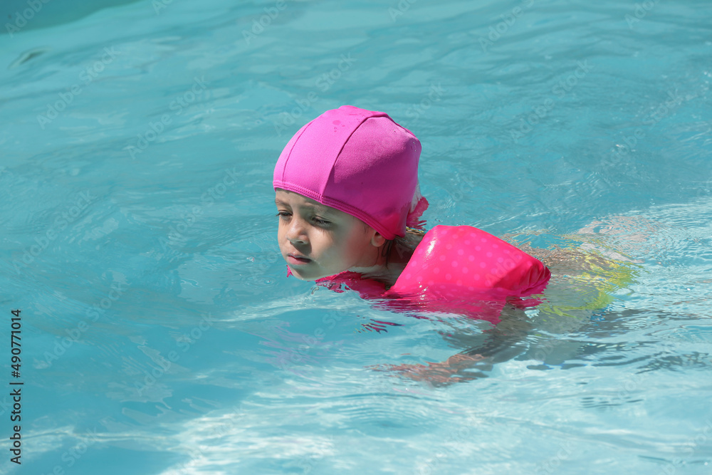 Criança na piscina nadando com flutuador rosa com água azul.