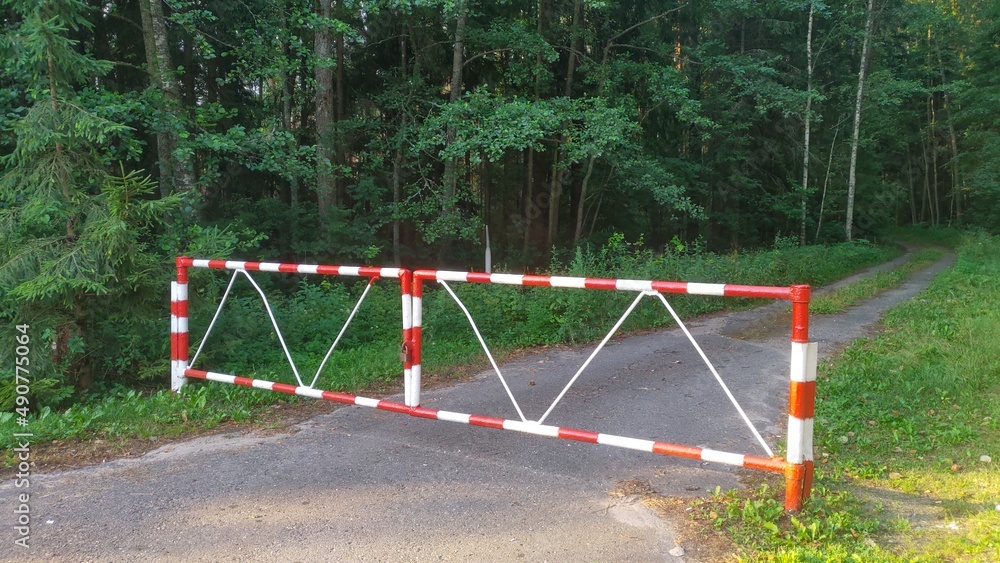 The metal gates at the exit from the paved highway to the forest dirt road are locked. This is done during the summer dry and fire-hazardous period to prevent forest fires. Grass and trees grow along The metal gates at the exit from the paved highway to the forest dirt road are locked. This is done during the summer dry and fire-hazardous period to prevent forest fires. Grass and trees grow along