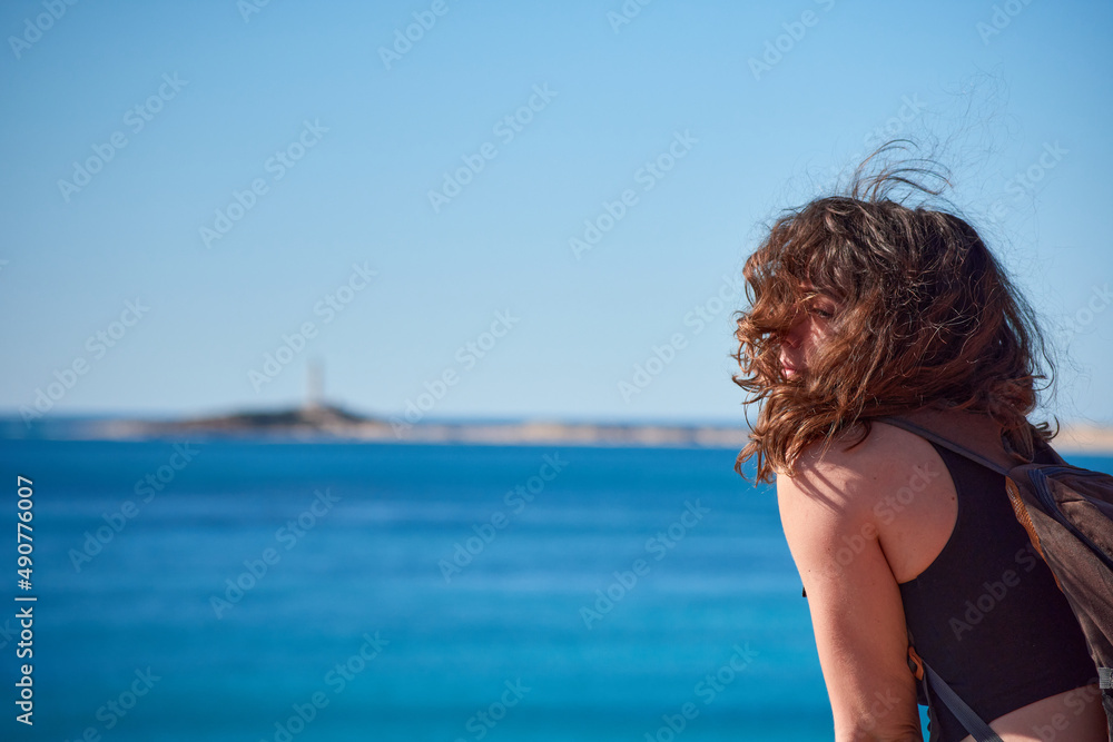 A closeup of a woman from behind looking at the Trafalgar lighthouse in the distance