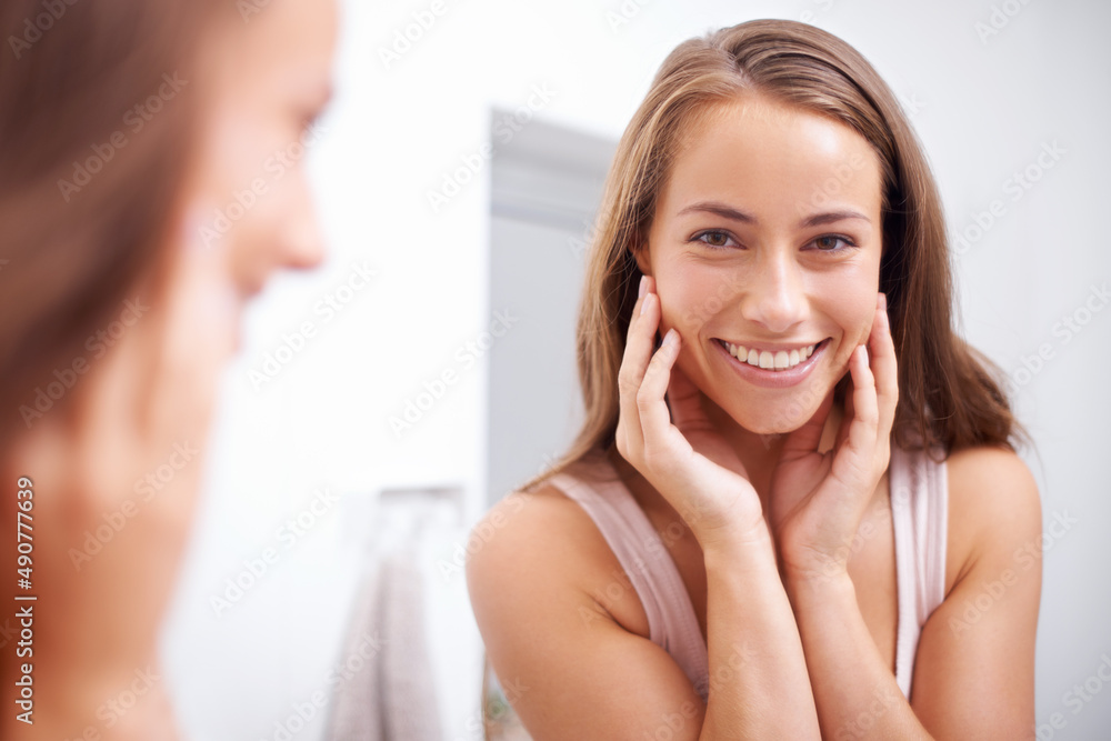 Shes the fairest of them all. A young woma touching her face happily as she looks in the mirror. Shes the fairest of them all. A young woma touching her face happily as she looks in the mirror.