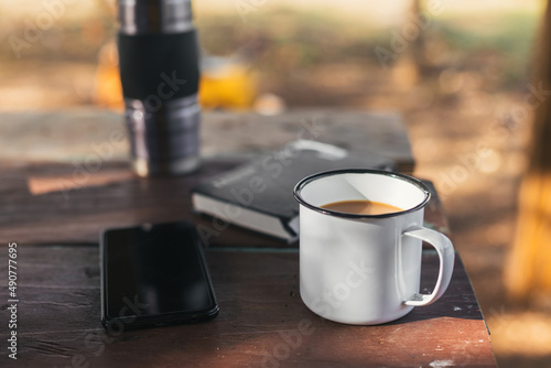 cup of coffee on the table with the mobile and a thermos, in a natural environment