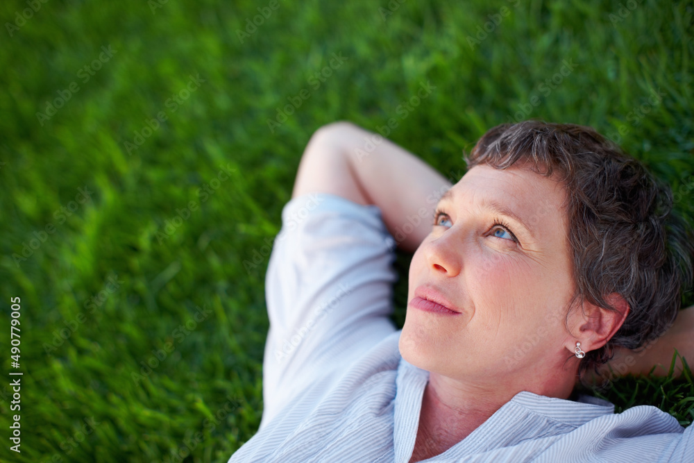 Woman relaxing outdoors. Closeup of thoughtful mature woman relaxing while lying on grass. Woman relaxing outdoors. Closeup of thoughtful mature woman relaxing while lying on grass.