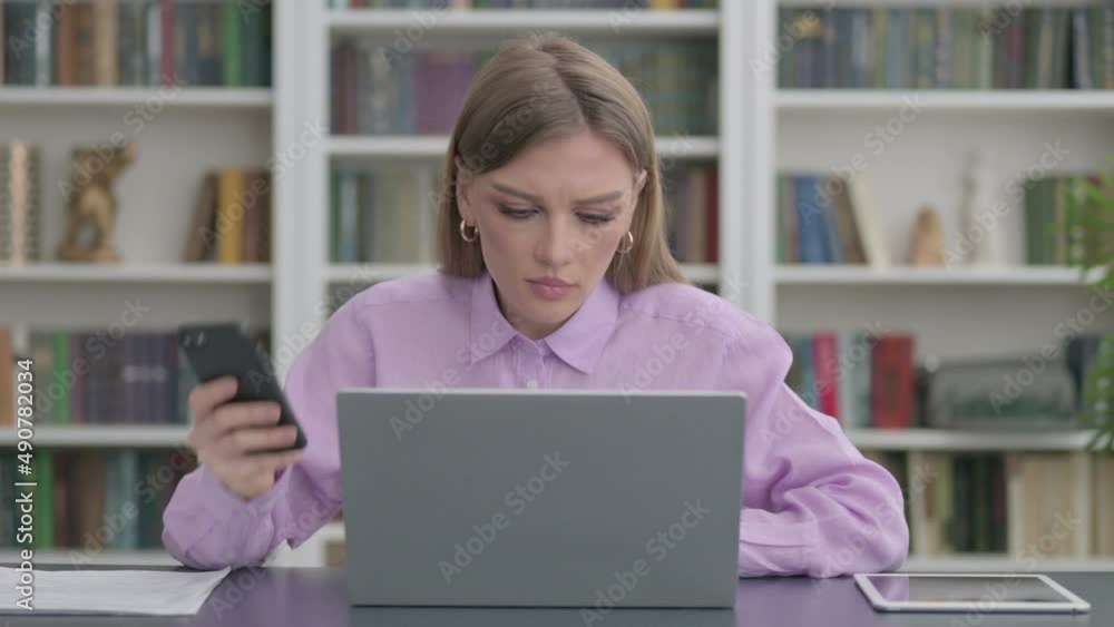 Woman using Smartphone while using Laptop in Office Woman using Smartphone while using Laptop in Office