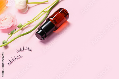 Bottle of cosmetic product, false eyelashes and ranunculus flowers on pink background, closeup
