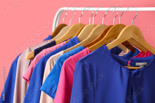 Rack with clean colorful clothes on pink background, closeup