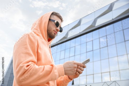 Young guy in stylish hoodie and with phone outdoors