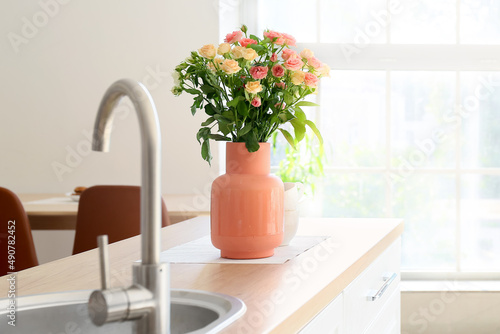 Beige vase with beautiful roses on counter in kitchen