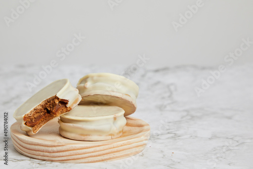 Argentinean white chocolate alfajores with dulce de leche on a wooden plate on a marble table.