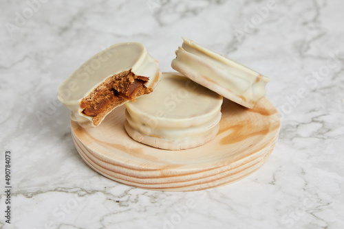Argentinean white chocolate alfajores with dulce de leche on a wooden plate on a marble table.