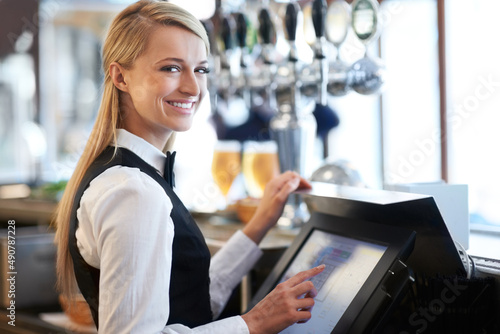 I am a whiz on this till. Beautiful barmaid standing by a till smiling as she rings through a round of drinks. photo