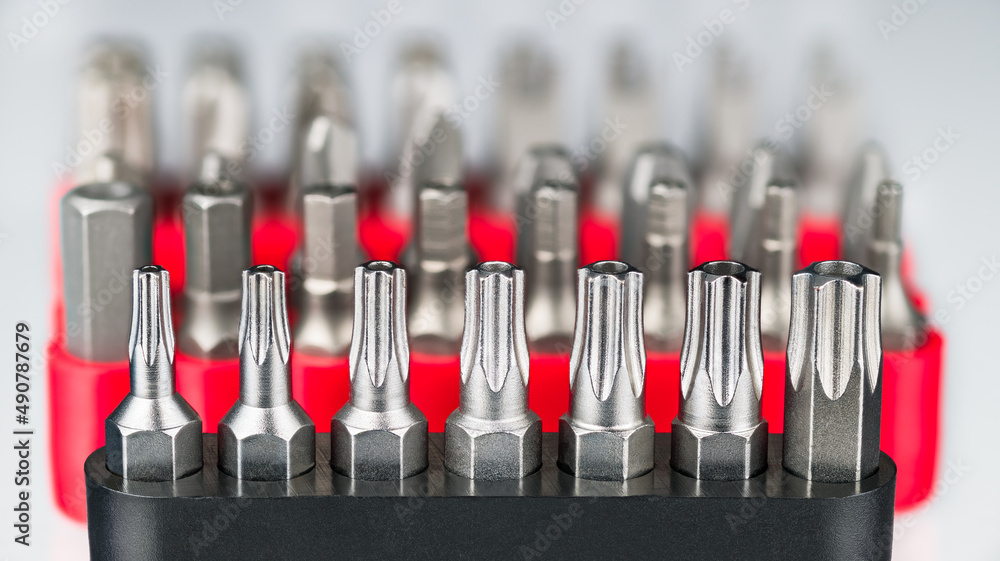 Fototapeta premium Closeup of metal torx, hexagon or pozidriv screwdrivers toolkits on white blurry background. Steel star bits set and different screw drivers kit of varied sizes in black or red box in artistic detail.