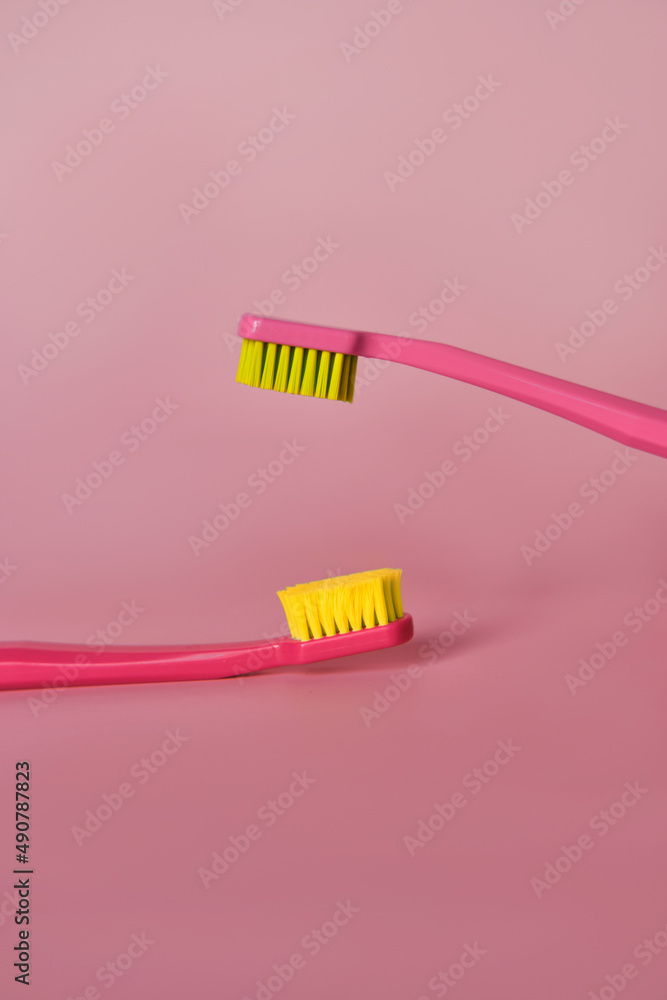 Two pink toothbrushes stand in pink glass on pink background. One brush is new and other has been used. Yellow bristles are disheveled, green bristles are new. Two pink toothbrushes stand in pink glass on pink background. One brush is new and other has been used. Yellow bristles are disheveled, green bristles are new.