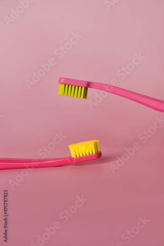 Two pink toothbrushes stand in pink glass on pink background. One brush is new and other has been used. Yellow bristles are disheveled  green bristles are new.