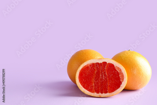 Tasty ripe grapefruits on purple background