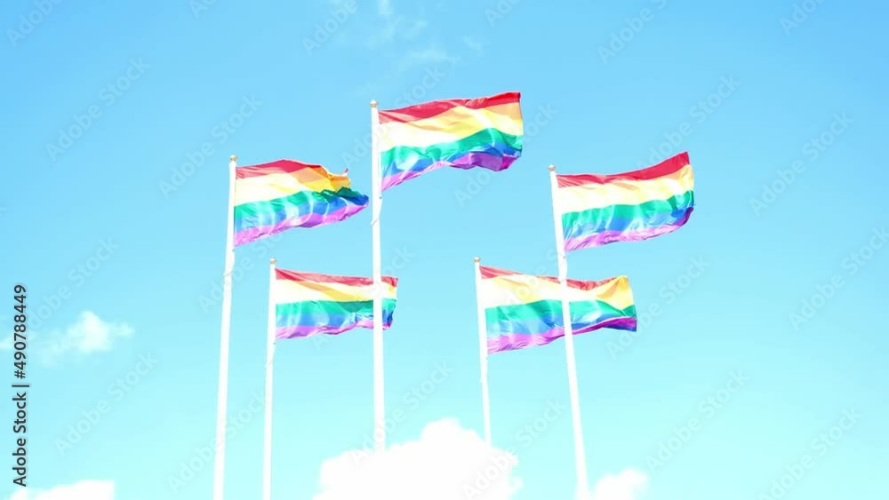 Rainbow flags waving in the wind against blue sky with clouds, sunny day Rainbow flags waving in the wind against blue sky with clouds, sunny day