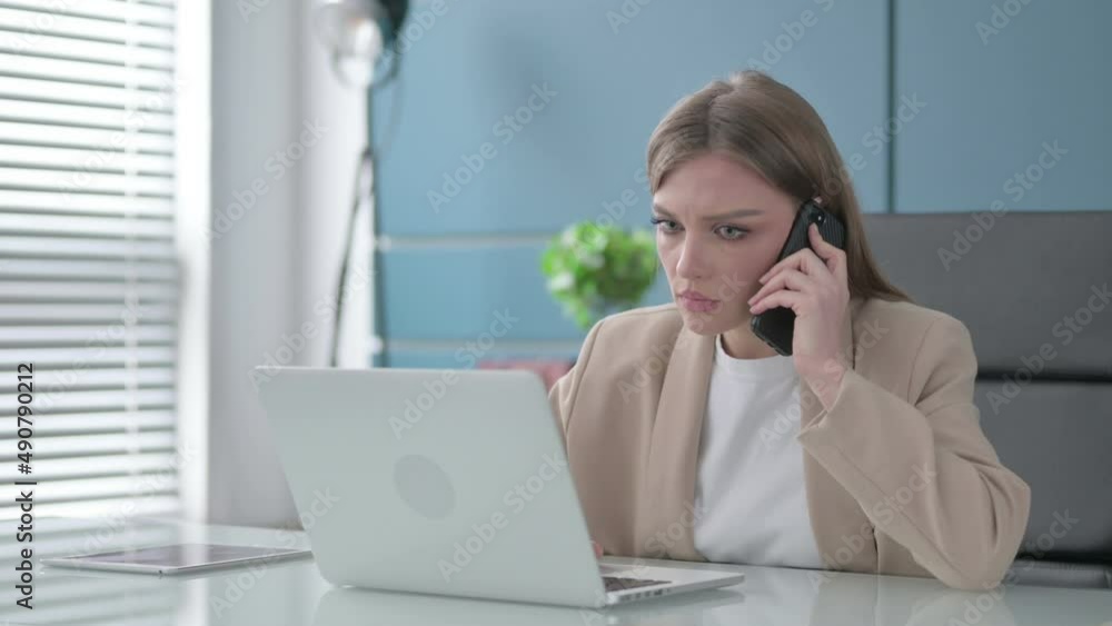Businesswoman Talking on Smartphone while using Laptop in Office Businesswoman Talking on Smartphone while using Laptop in Office