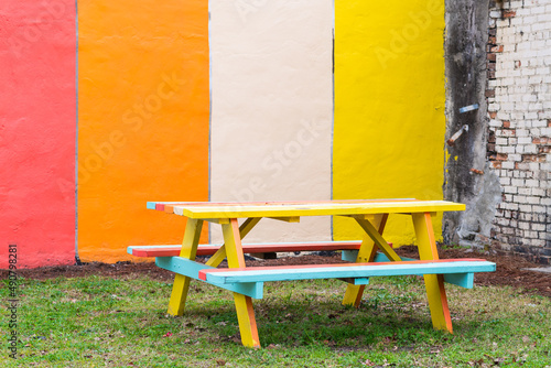 Murais de parede Colorful picnic table with benches on the grass against a painted wall