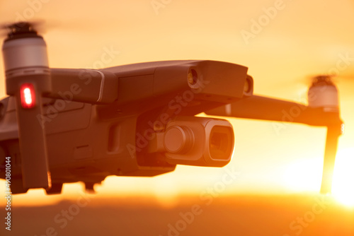 Unmanned quadcopter in flight with a digital camera at sunset. Drone silhouette at sunset © Vladyslav