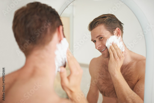 For a smooth shave.... A handsome young man applying shaving cream to his face in front of a mirror.