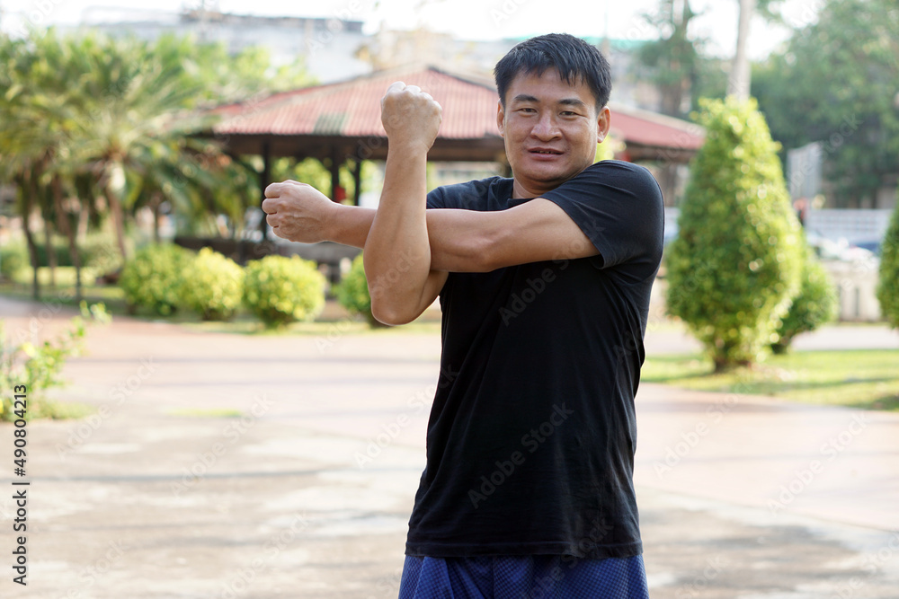 Portrait of Asian man is exercising in the park. Shoulder stretch. Concept : Healthy lifestyle. Full body stretching. ฺBurn fat and calories. Exercise is good for physical and mental health.