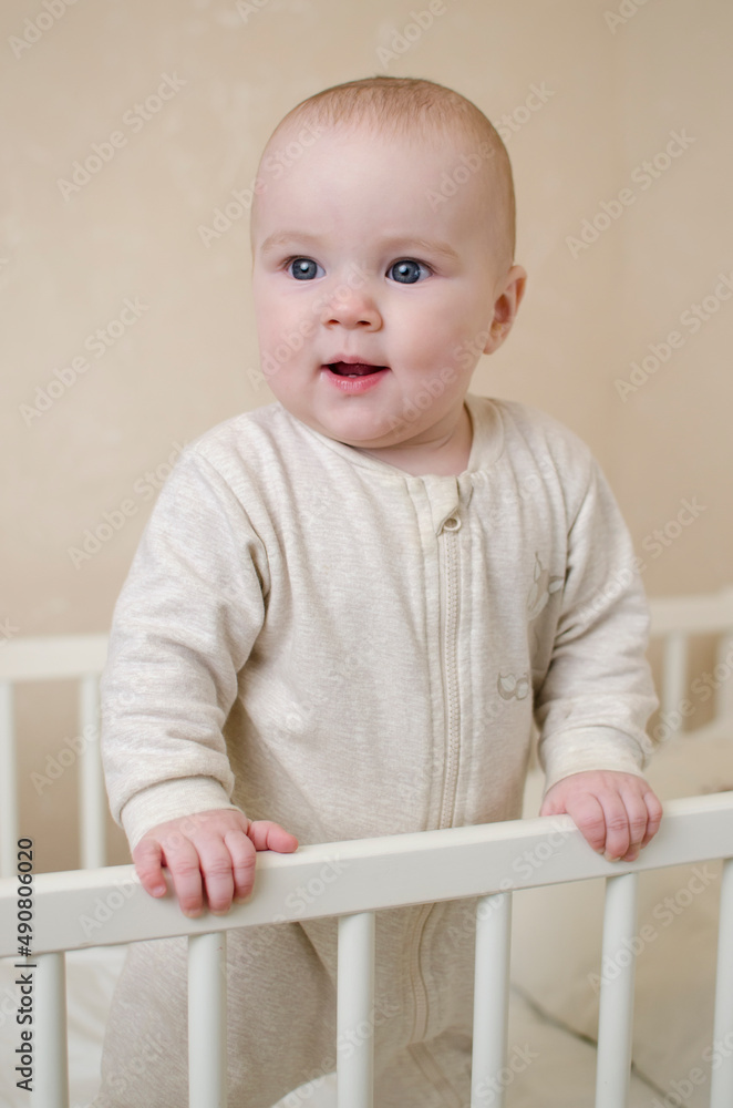 Portrait of a little smiling infant baby girl standing in a crib in the bedroom of the house. Teeth cut, salivation concept Portrait of a little smiling infant baby girl standing in a crib in the bedroom of the house. Teeth cut, salivation concept