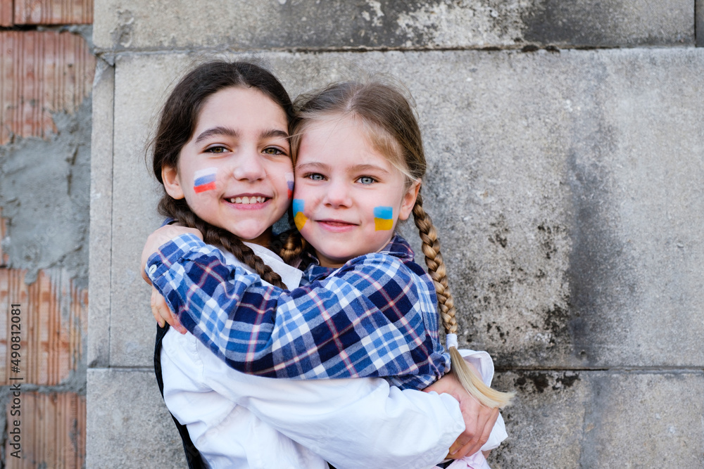 Portrait of two little girls embracing with Russian and Ukrainian flags on the faces. Concept of peace, stop the war and friendship of children against hate people Portrait of two little girls embracing with Russian and Ukrainian flags on the faces. Concept of peace, stop the war and friendship of children against hate people