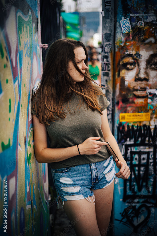 Naklejka premium Young and beautiful woman leans against a colorful wall and poses for the camera - typical street style