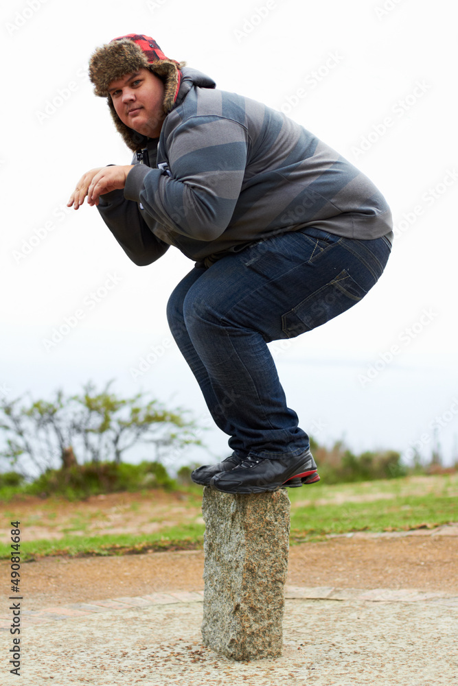 Ready to pounce. An overweight young man in winter wear balancing playfully on a post. Ready to pounce. An overweight young man in winter wear balancing playfully on a post.