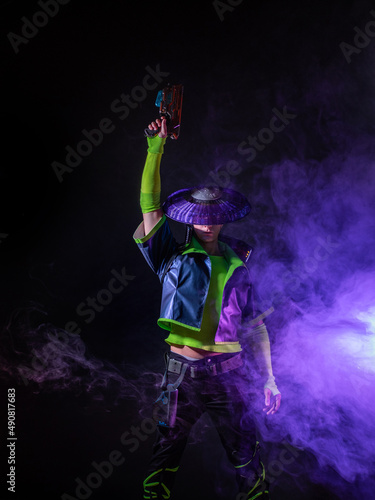 Futuristic character in a bright stylized outfit, fires a blaster. photo with neon colors. A fantastic character, a cyber mercenary