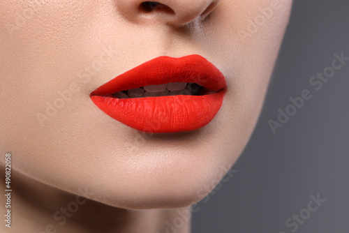 Young woman with beautiful red lips on grey background  closeup