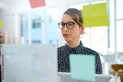 You shouldnt ignore the planning process. Shot of a young businesswoman using a digital tablet while brainstorming with notes on a glass wall in an office. photo