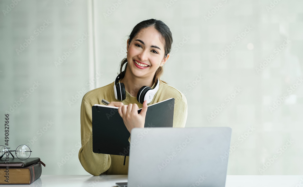 Asian student girl education study abroad looking to camera, holding book while learning online via laptop. Asian student girl education study abroad looking to camera, holding book while learning online via laptop.