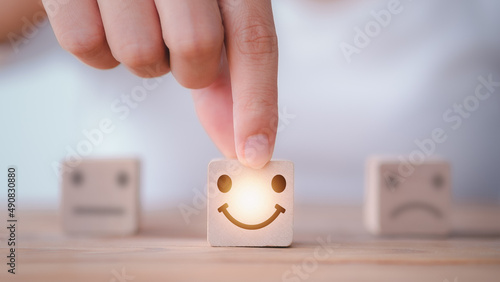 Customer service satisfaction survey concept. Customer hand choose happy smiley face, blurred neutral and sad face icon on wood cube to survey feedback, business, rating, review, service satisfaction.