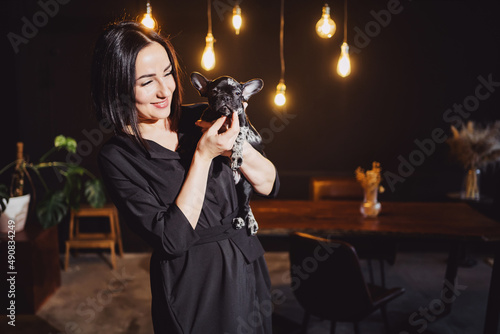 attractive brunette woman with French Bulldog puppy in dark loft-style apartment