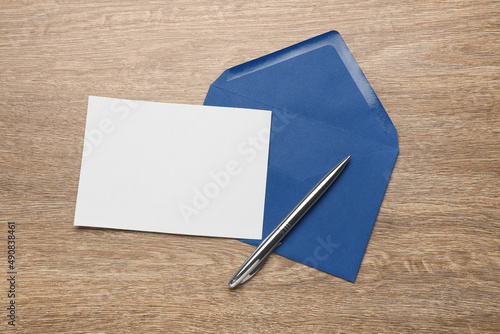 Blue envelope with blank letter and pen on wooden table, flat lay