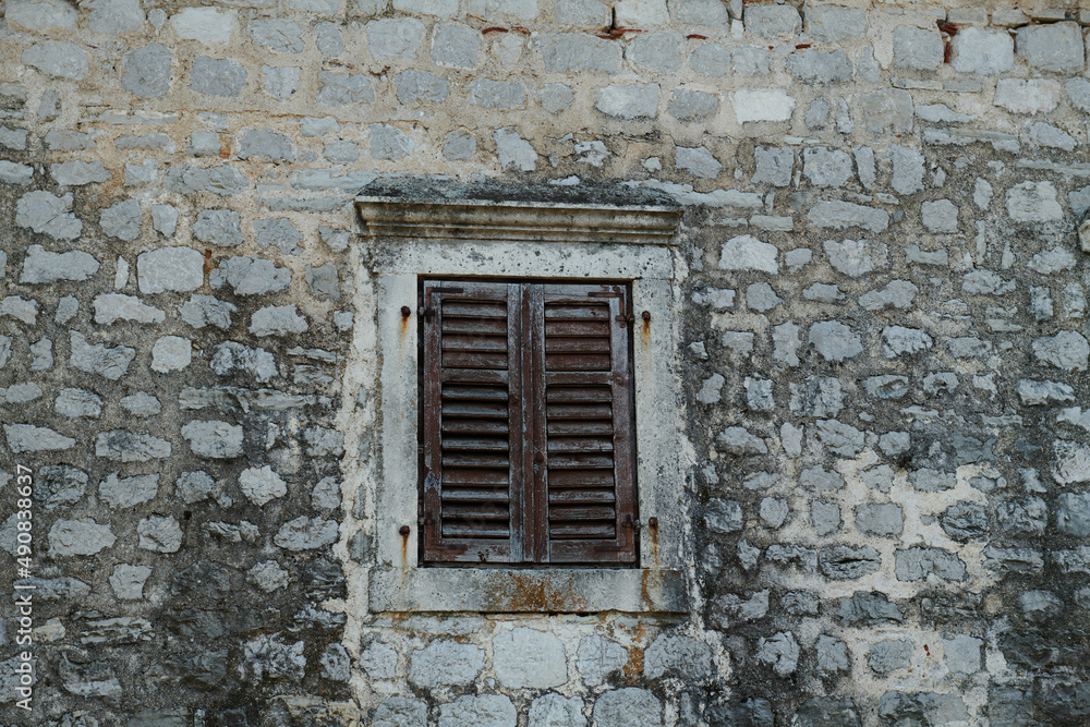 the stone wall is old and the window with shutters