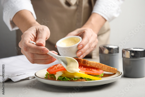 Woman making sandwich with mayonnaise at grey table, closeup photo