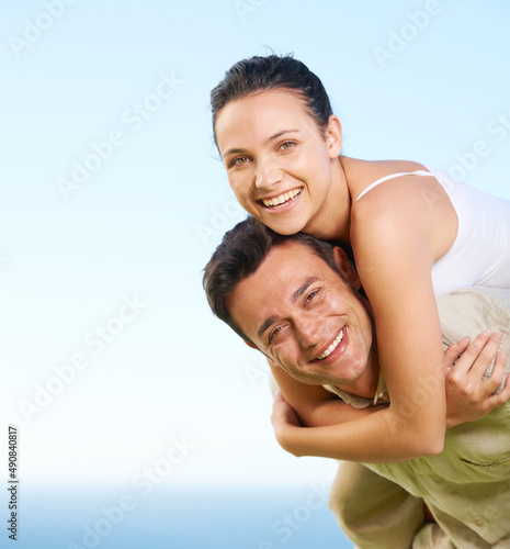 Enjoying their holiday. A young man giving his girlfriend a piggyback with the ocean in the background.