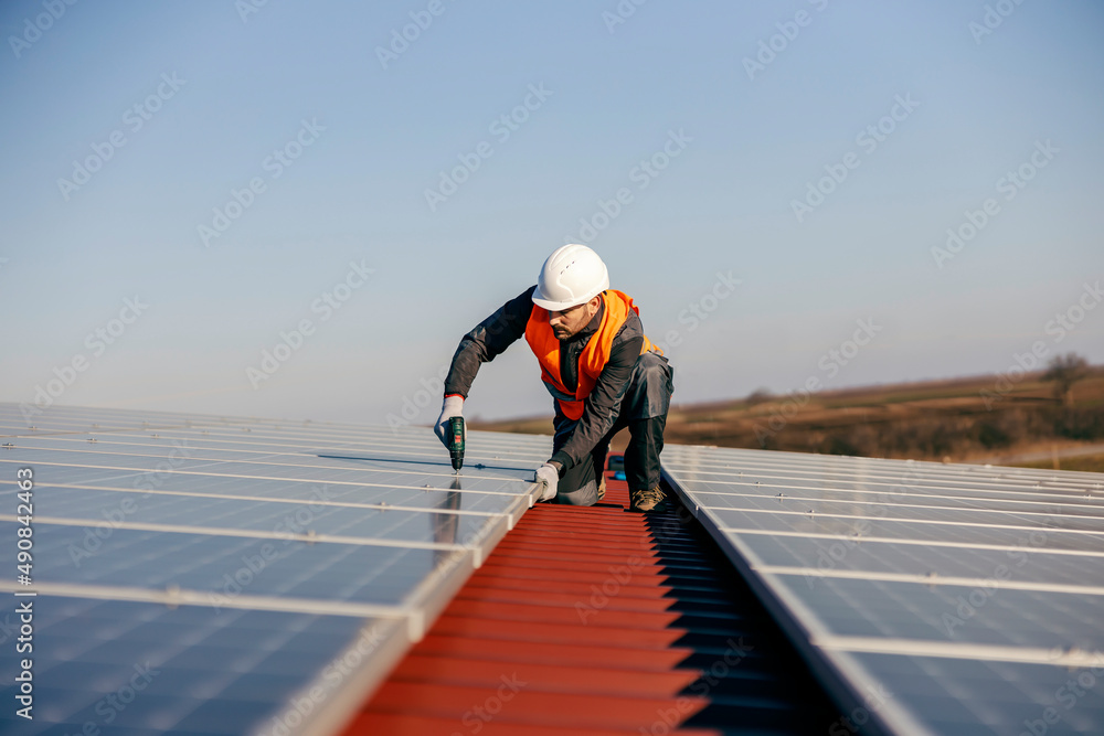 A handyman kneeling on the roof and installing solar panels.