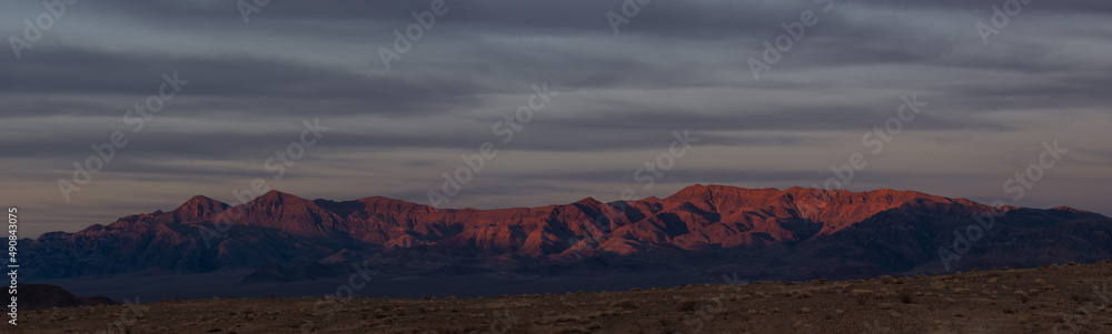 Desert landscape of the Nopah range in Inyo County, California. This panoramic image was taken at dusk and shows a sky with clouds and muted colors.